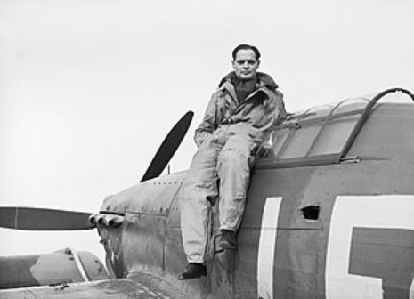A pathfinder wearing a flight suit sits on the wing of a propeller aircraft, poised for the next mission.